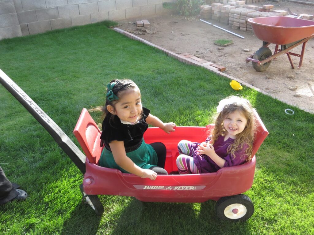 Two children play in a red wagon.